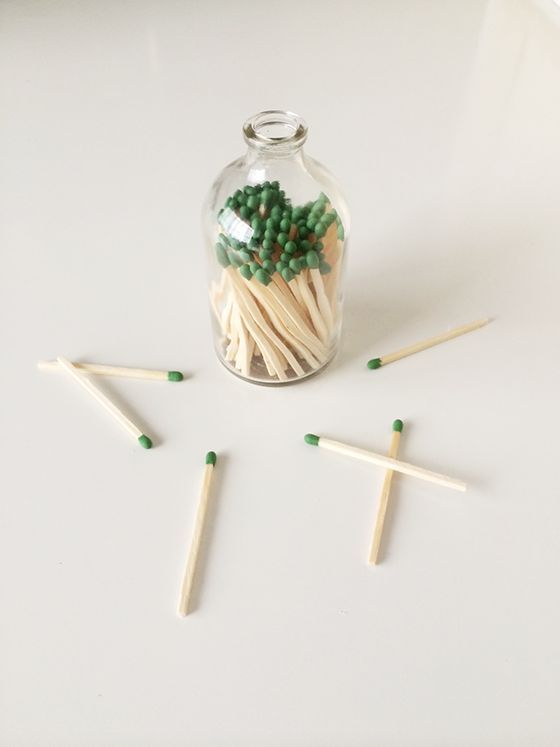 matchsticks in a glass jar with green and white matches on the ground next to them