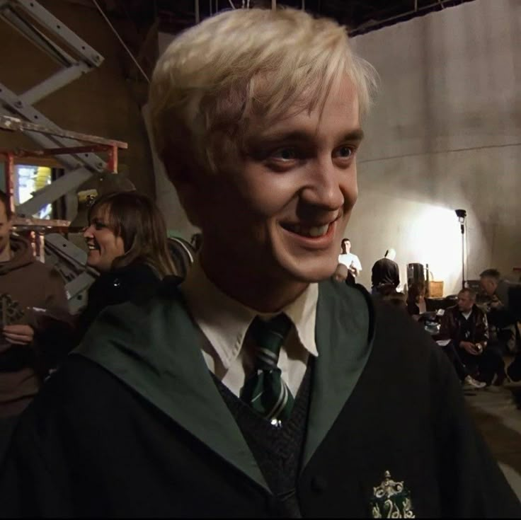 a man with blonde hair wearing a harry potter outfit and smiling at the camera while others look on