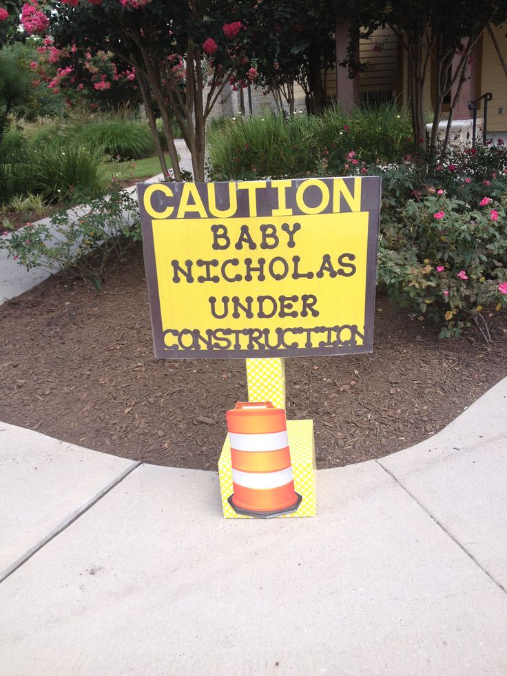 a caution sign in front of a tree and bushes with flowers around it that reads, baby nicholas under construction