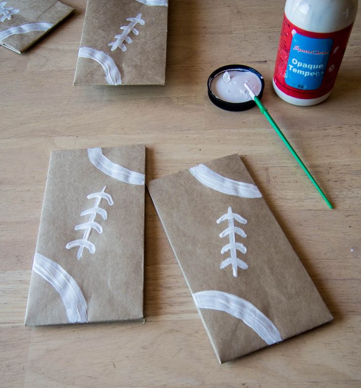 paper bags with footballs painted on them sitting on a table next to glue and toothbrush