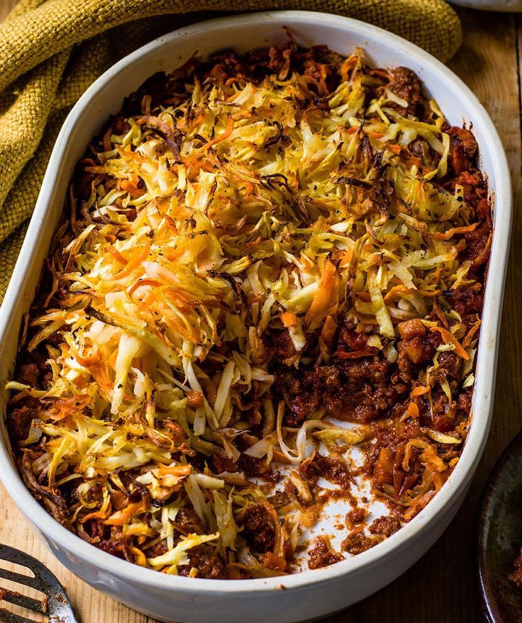 a casserole dish filled with shredded cheese and ground beef, on a wooden table