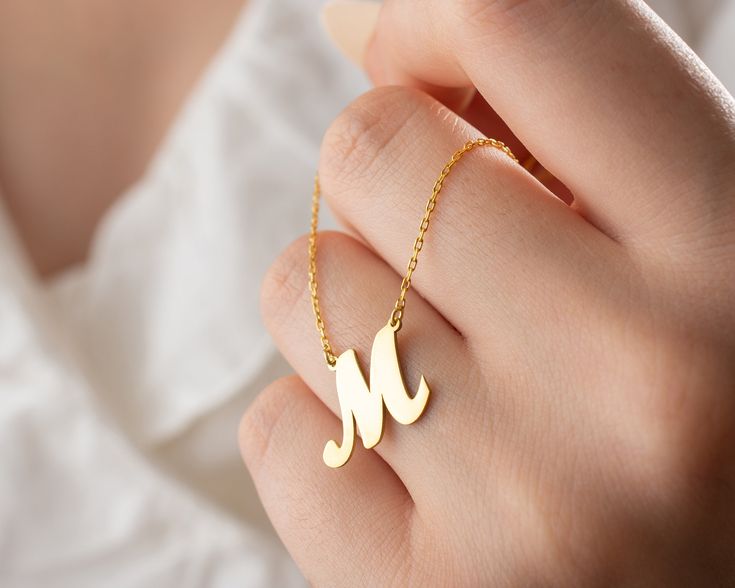 a woman's hand holding a gold necklace with the letter m on it