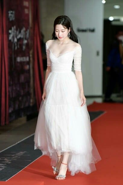 a woman in a white dress walking down a red carpeted floor with her hand on her hip