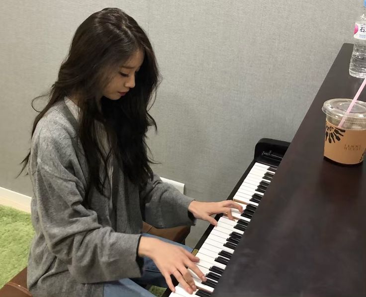 a woman sitting at a piano with a drink in her hand and playing the piano