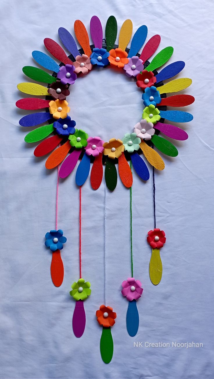 a colorful wind chime hanging from a white wall with flowers and leaves on it