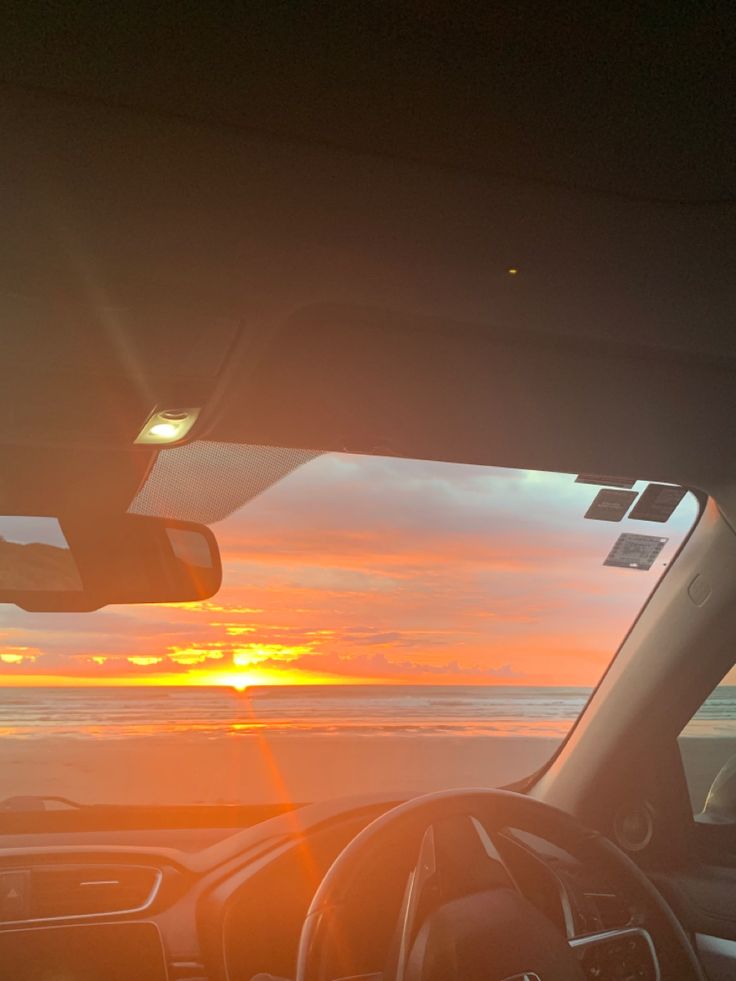 the sun is setting over the ocean as seen from inside a car with dashboard lights on