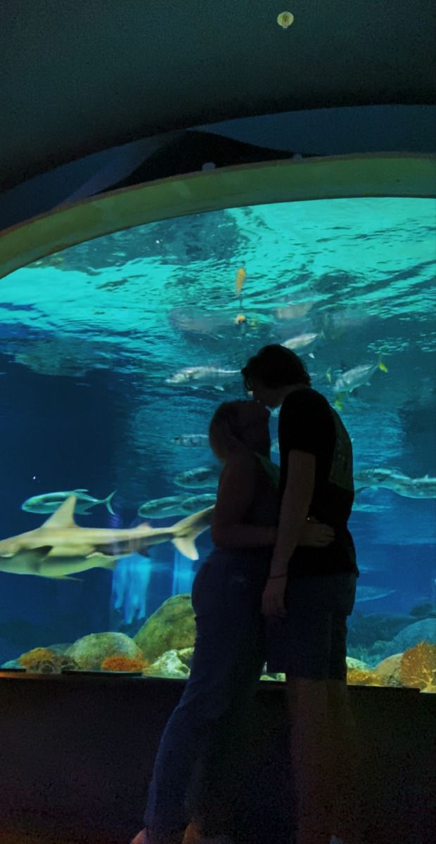 two people kissing in front of an aquarium