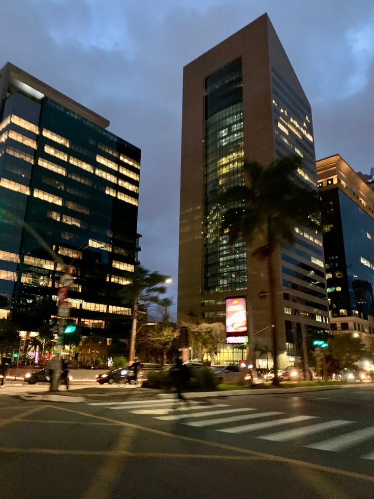 two tall buildings sitting next to each other on a city street at night with palm trees in the foreground