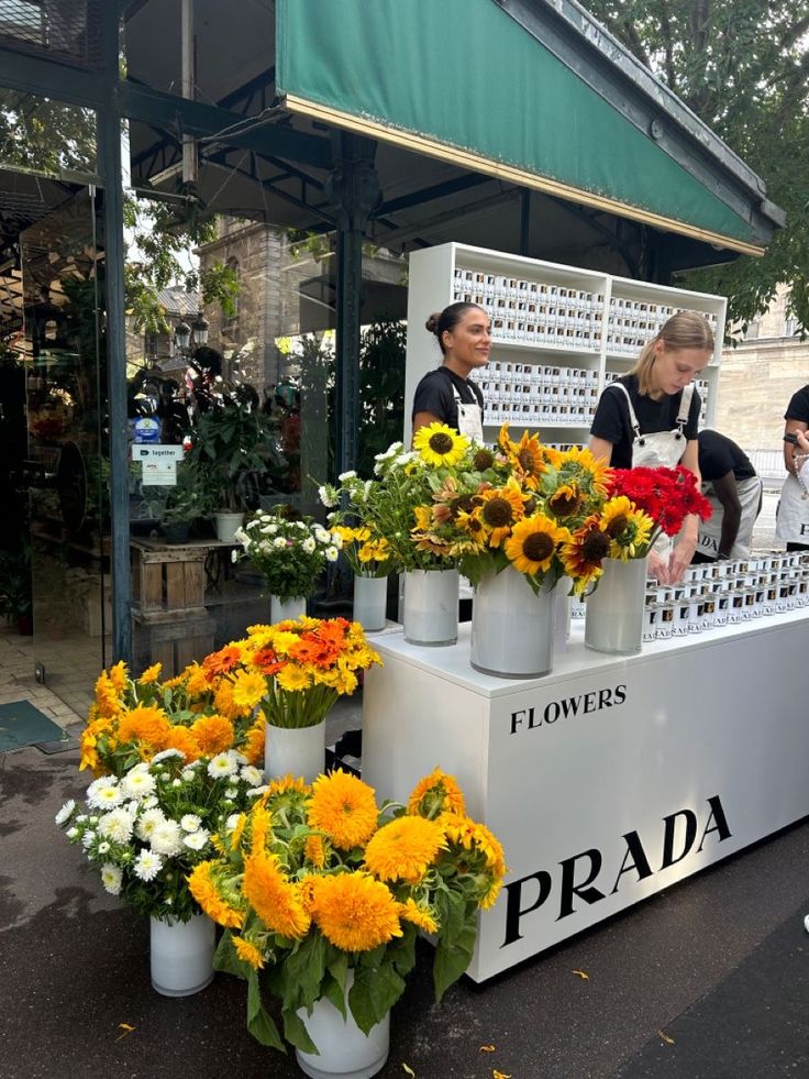 two women standing behind a flower stand selling flowers