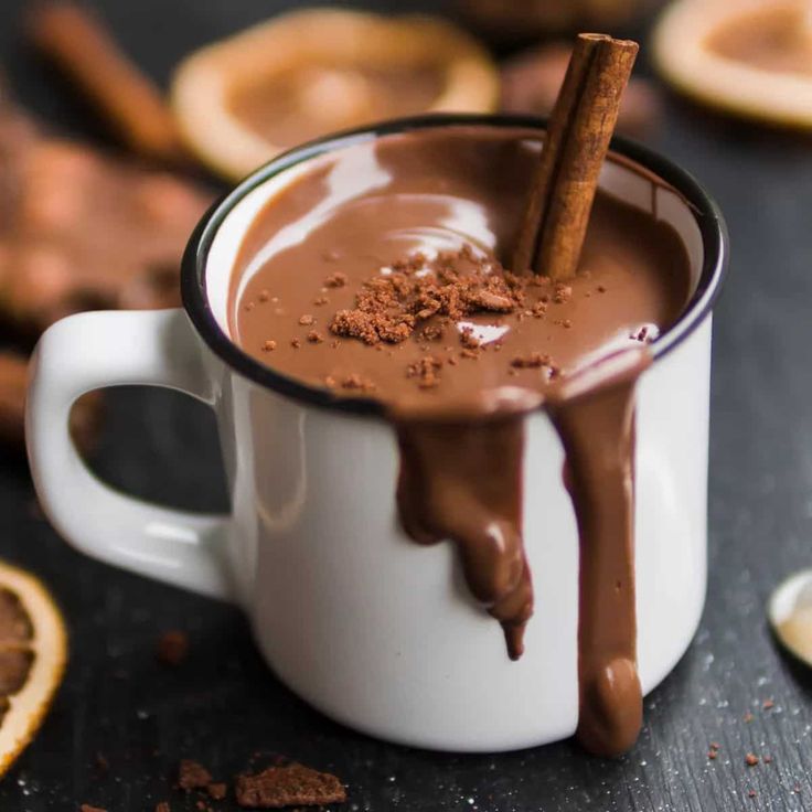 a mug filled with hot chocolate and cinnamon on top of a table next to sliced oranges