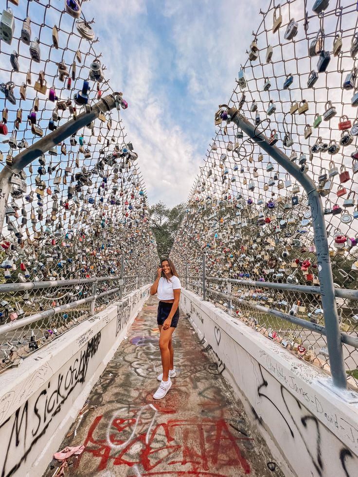 a woman walking across a bridge covered in lots of locks and chains, with the sky above her