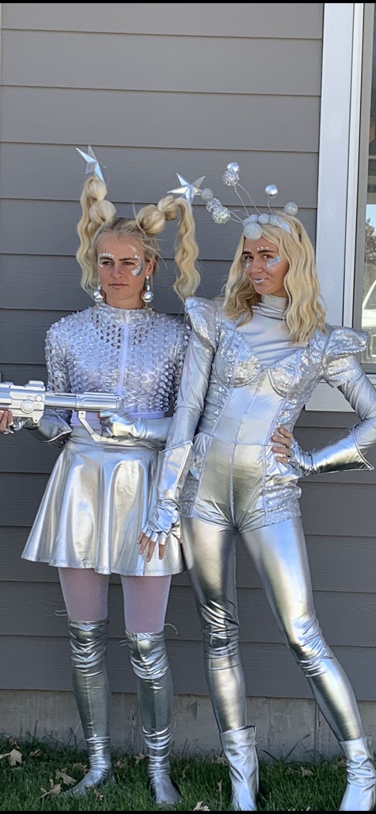 two women dressed in silver standing next to each other on the grass near a house