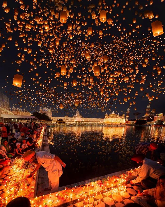 many people are flying lanterns over the water