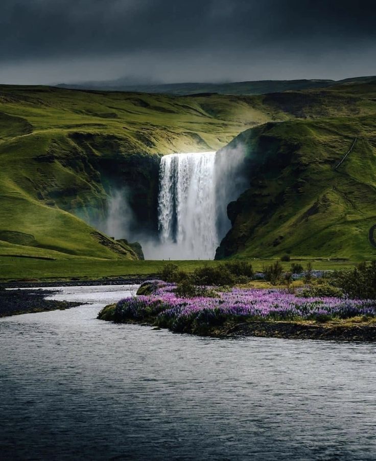 a large waterfall in the middle of a lush green field next to a body of water