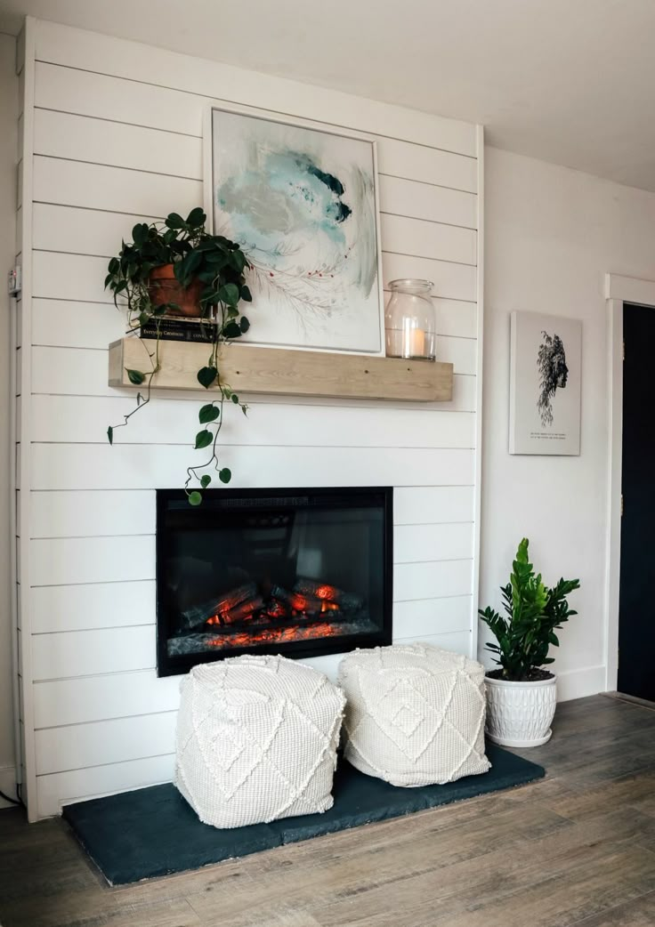 a fireplace with two white poufces sitting on top of it next to potted plants