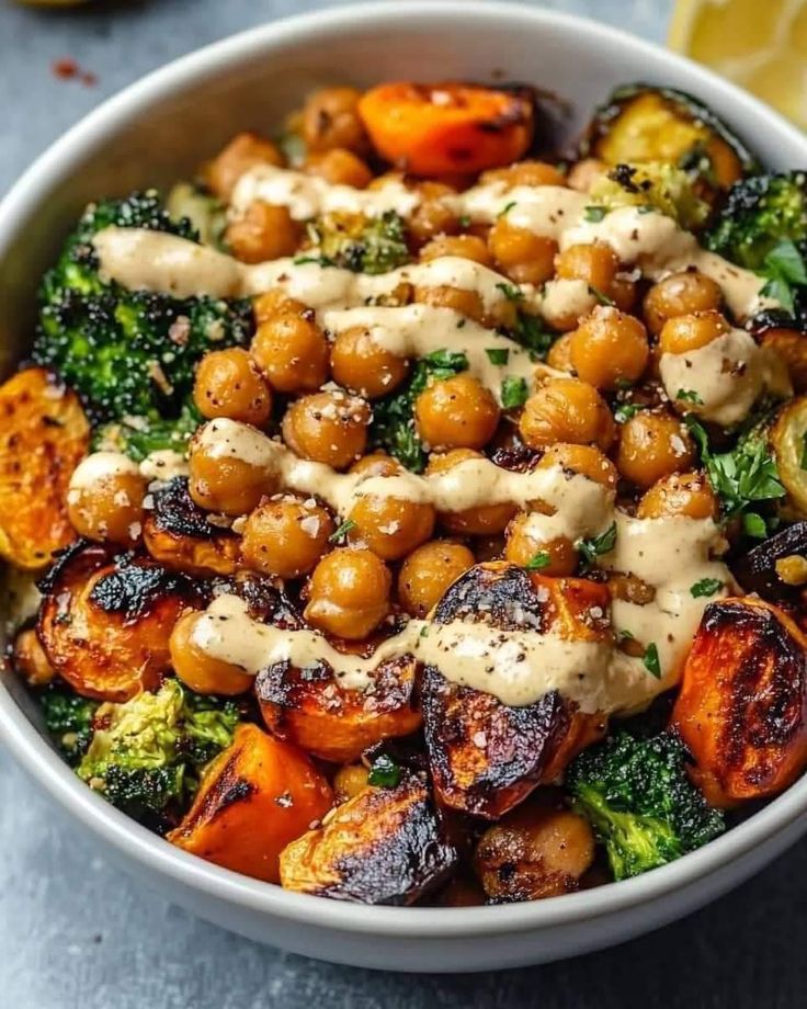 a white bowl filled with broccoli, chickpeas and carrots covered in sauce