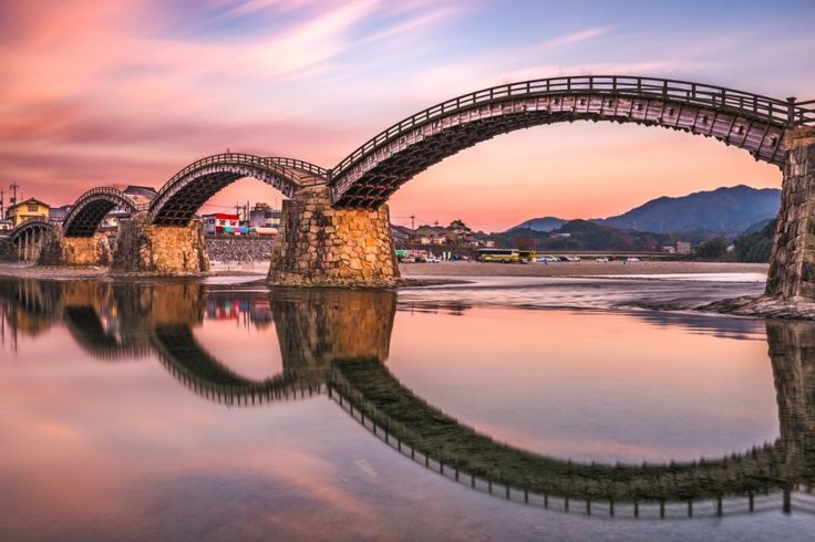 a bridge that is over water with mountains in the background and clouds in the sky