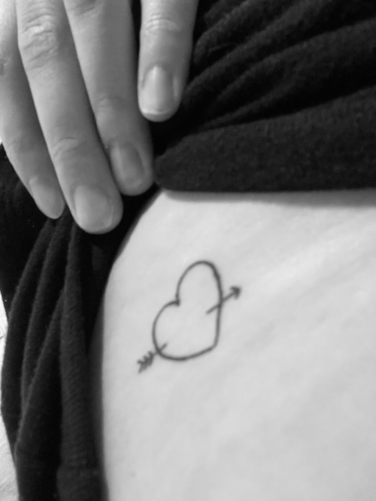 a woman's stomach with a heart and arrow tattoo on it