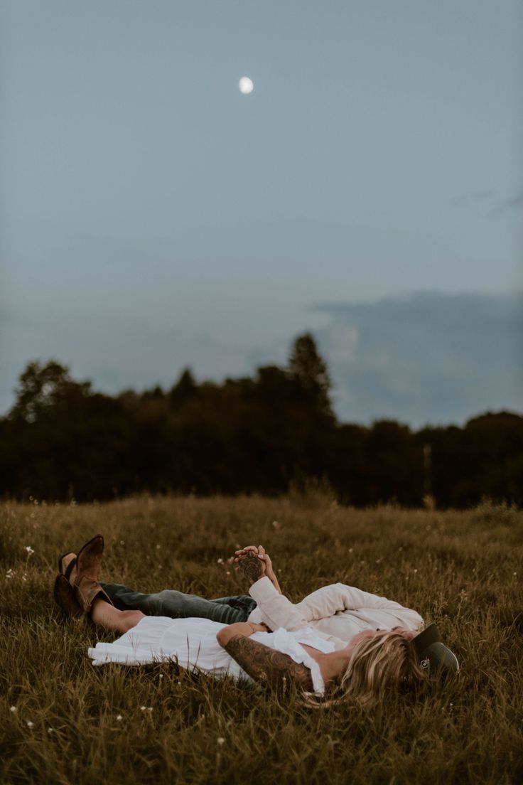 two people laying in the grass under a full moon