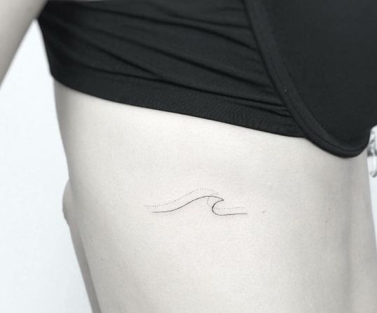 a woman's stomach with a small wave tattoo on it