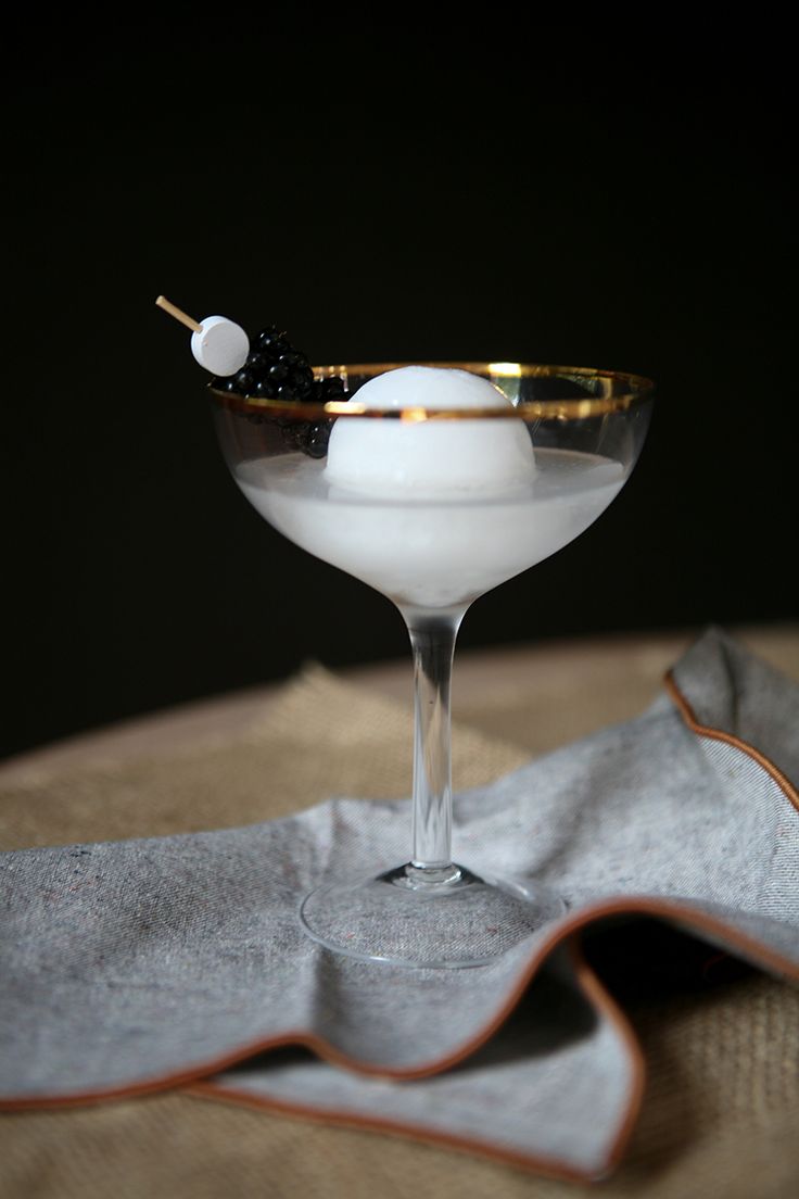 a martini glass with an olive garnish on the rim, sitting on a napkin