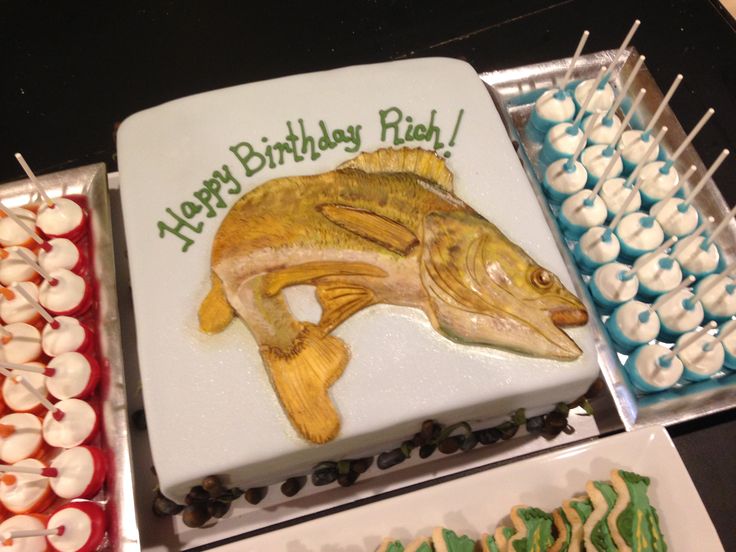 a birthday cake decorated with a fish on it's side and cupcakes in the background