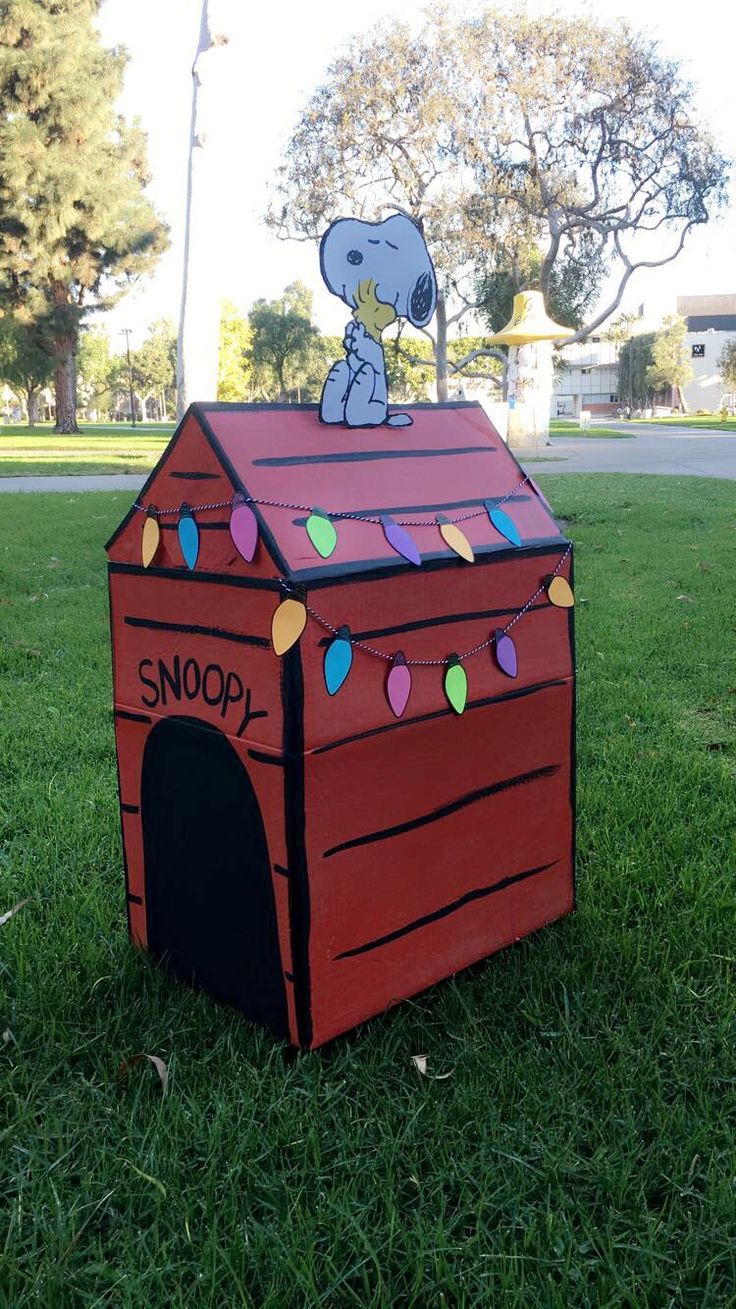 a dog house made out of cardboard with a snoopy on top and lights strung from the roof