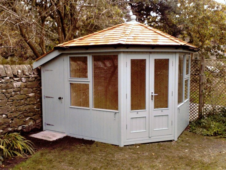 a small white outhouse sitting next to a stone wall and fenced in area