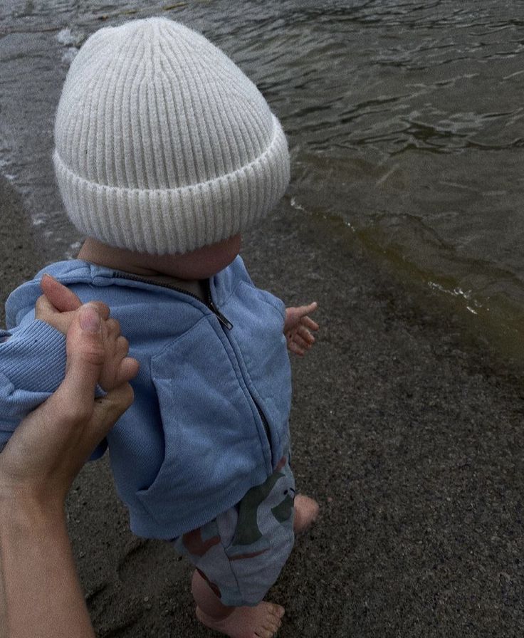 a person holding a baby in their arms near the water's edge while they are walking