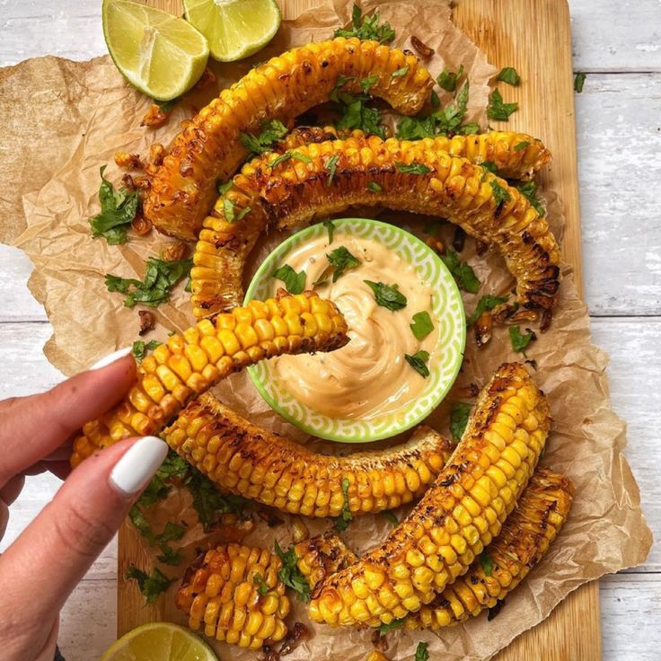 grilled corn on the cob with dipping sauce in a bowl and lime wedges