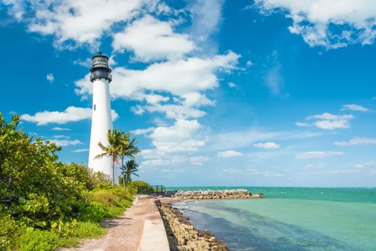 a white light house sitting on top of a lush green hillside next to the ocean