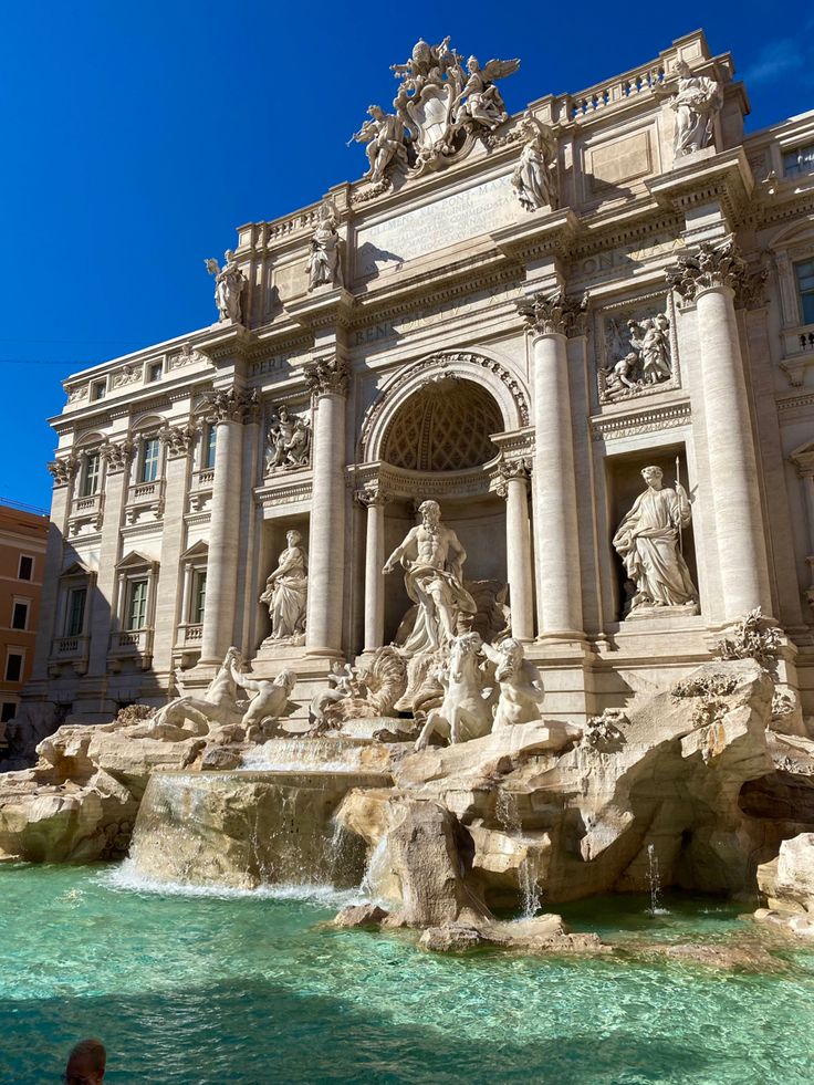 people are standing in front of a fountain with statues on the sides and water running down it