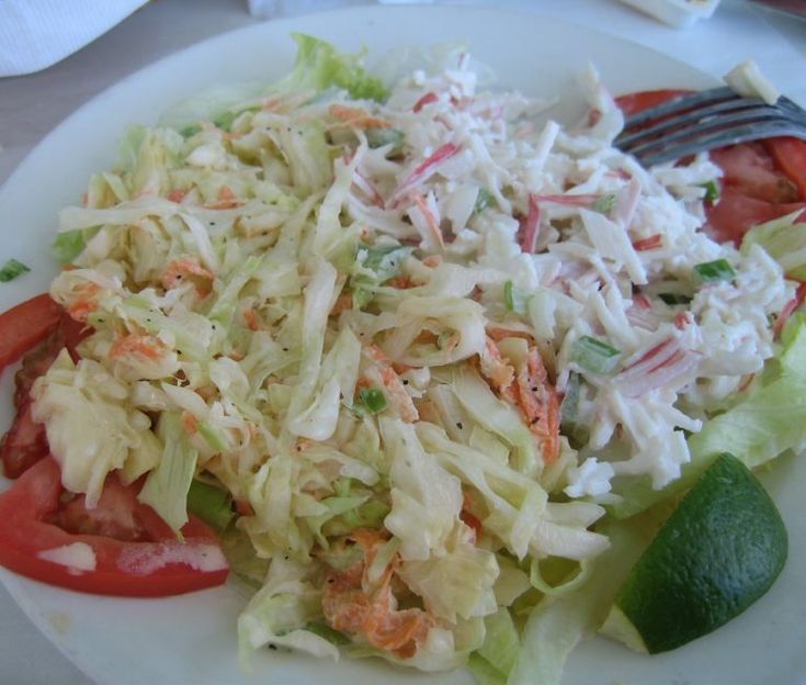 a white plate topped with lettuce, tomatoes and coleslaw next to a fork