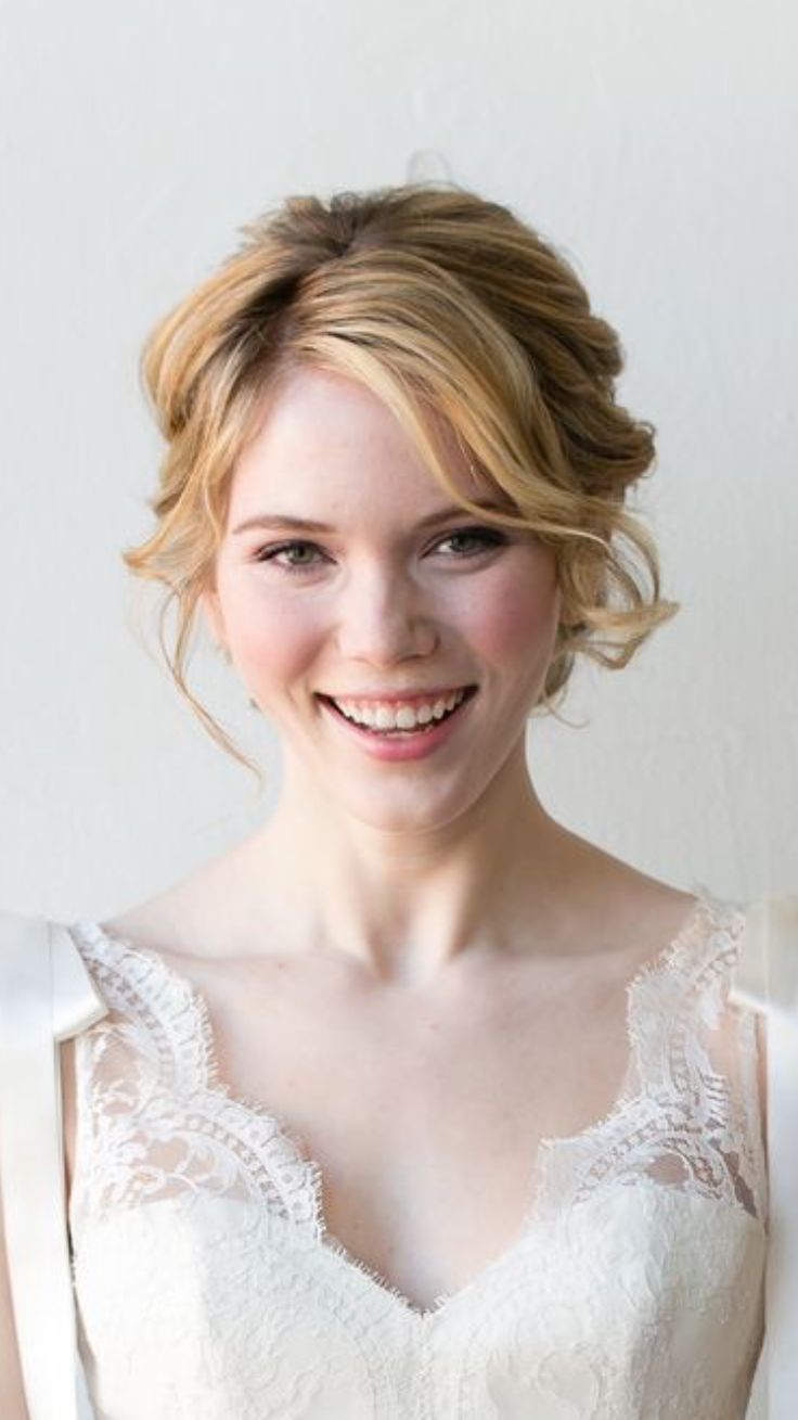 a woman with blonde hair wearing a white dress and smiling at the camera while standing in front of a wall