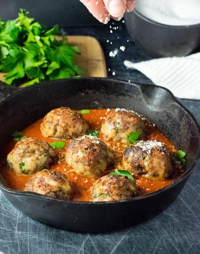 someone sprinkling parmesan cheese on some meatballs in a skillet