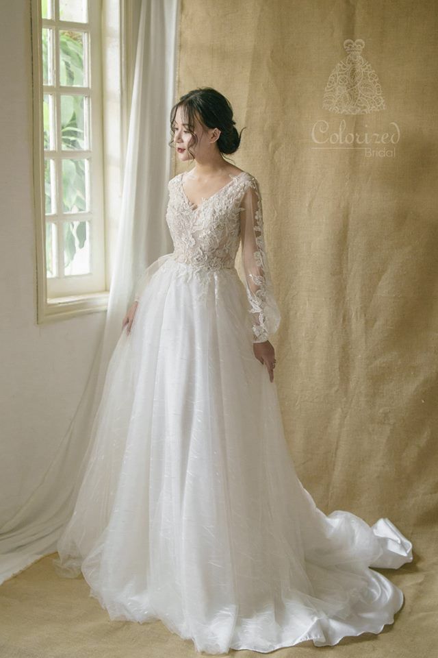 a woman standing in front of a window wearing a white wedding dress with long sleeves