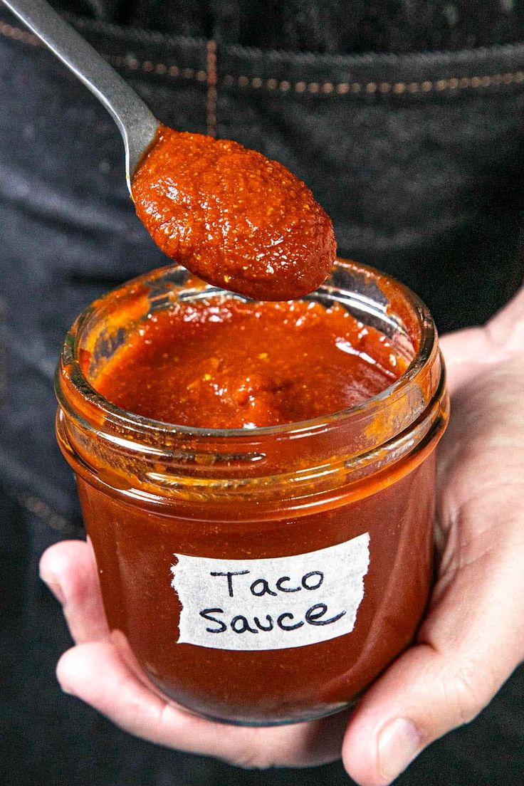 a person holding a spoon full of taco sauce in a jar with a tag on it