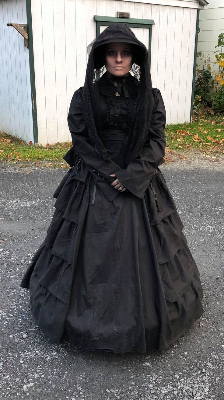 a woman in a black dress and bonnet is standing on the street with her hands behind her back