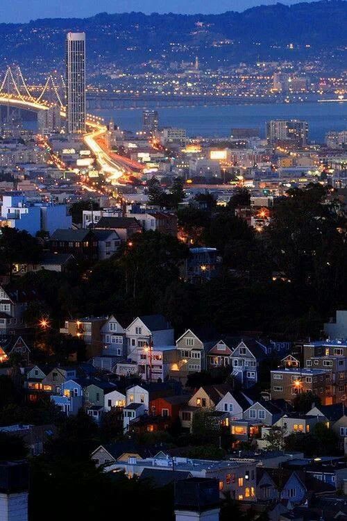 the city lights shine brightly in the night sky as seen from atop a hill with houses on it