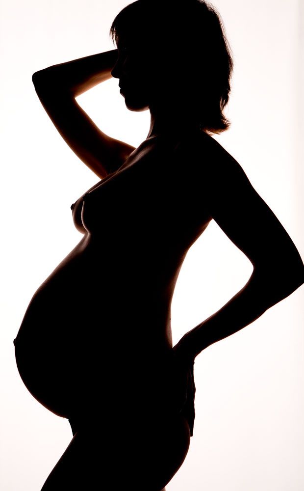 a pregnant woman posing in silhouette with her hands on her hips and arms behind her head