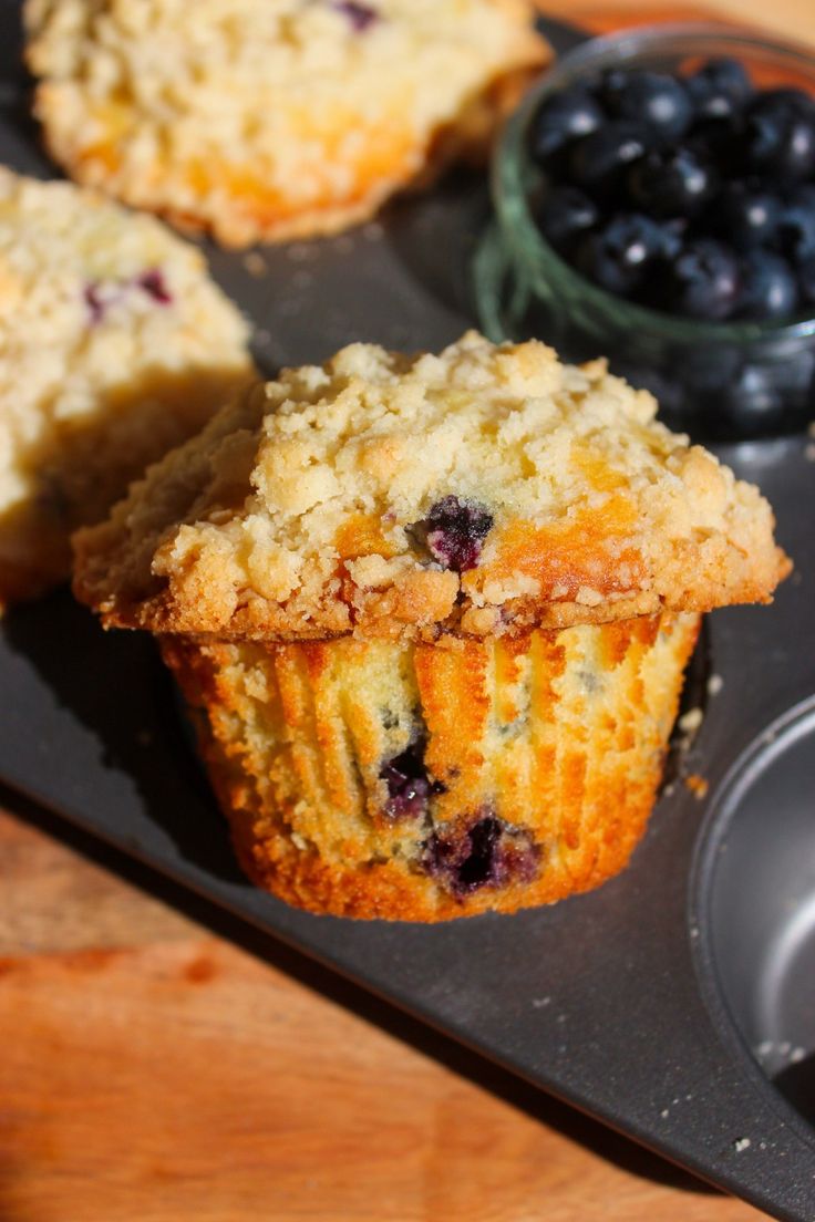 muffins and blueberries are sitting on a black tray next to a cupcake tin