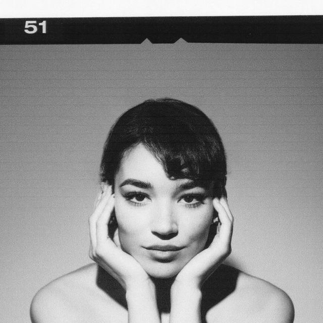 a black and white photo of a woman with her hands on her face, looking at the camera