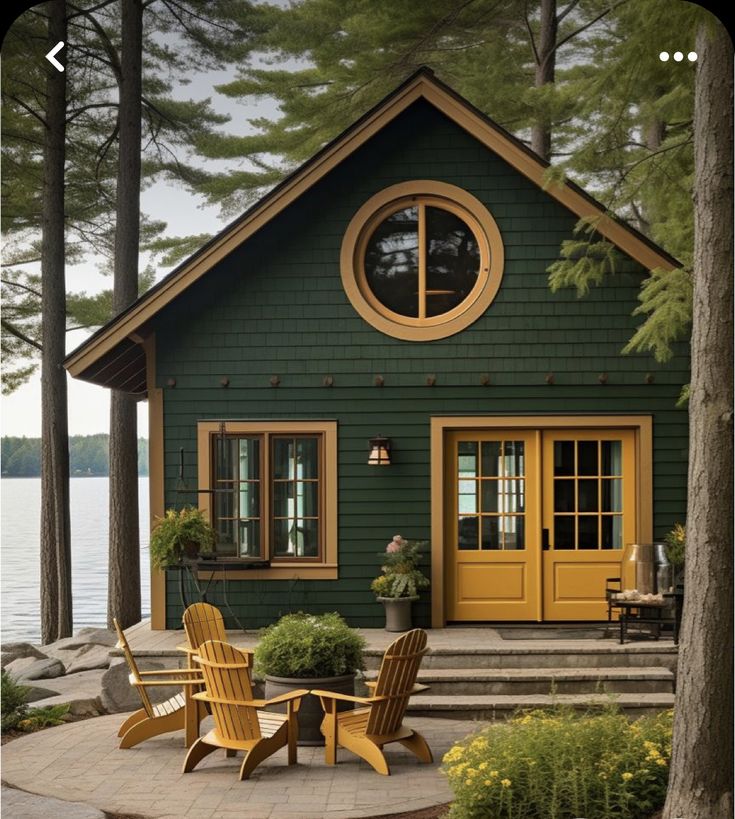 a green house with yellow doors and two chairs on the front porch next to it