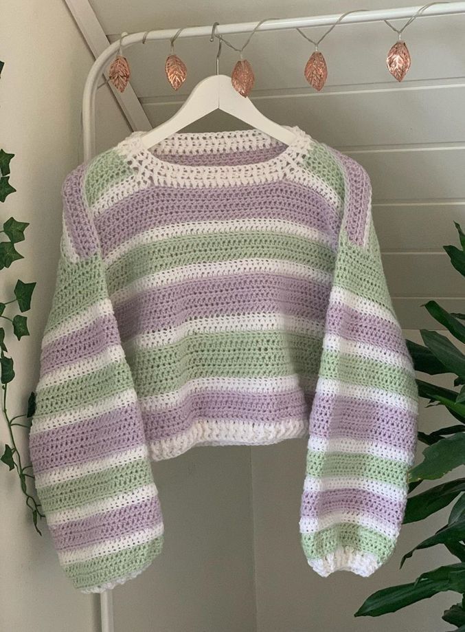 a crocheted sweater hanging on a clothes rack next to a potted plant