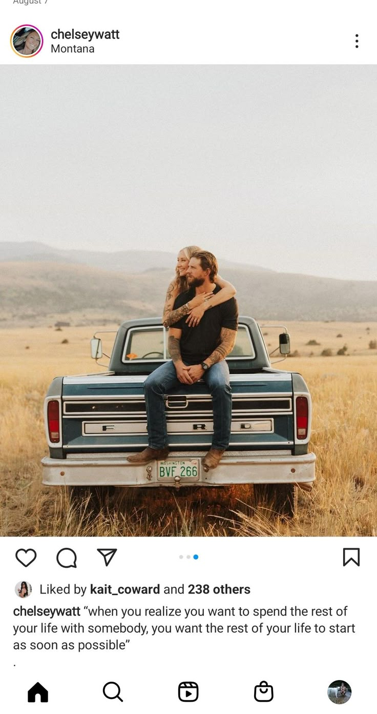 a man and woman sitting on the back of a pick up truck in an open field