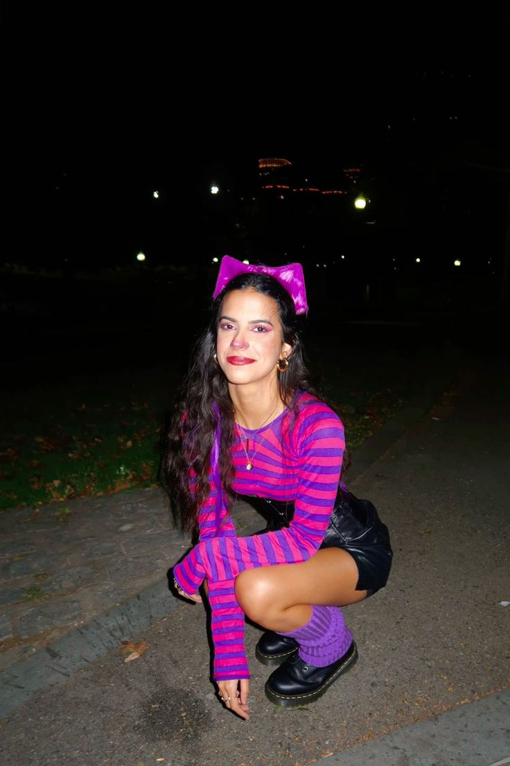 a woman in purple and black outfit kneeling down on the ground with her legs crossed