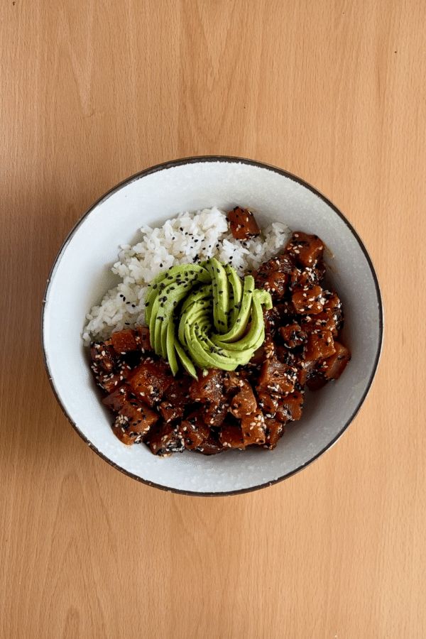 a bowl filled with rice, meat and avocado on top of a wooden table