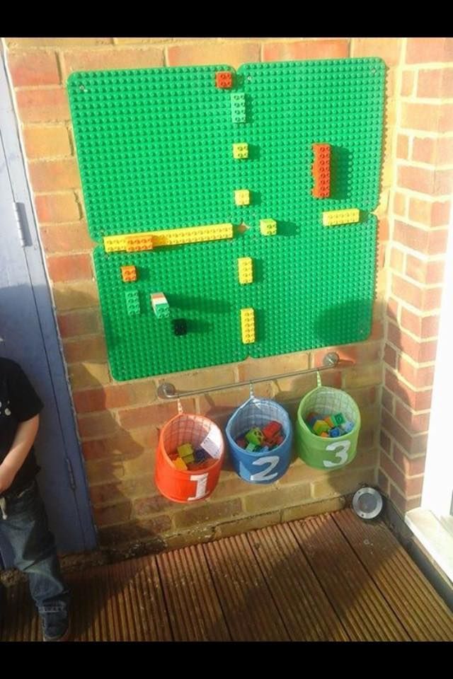 a young boy standing in front of a green lego wall hanging on a brick wall