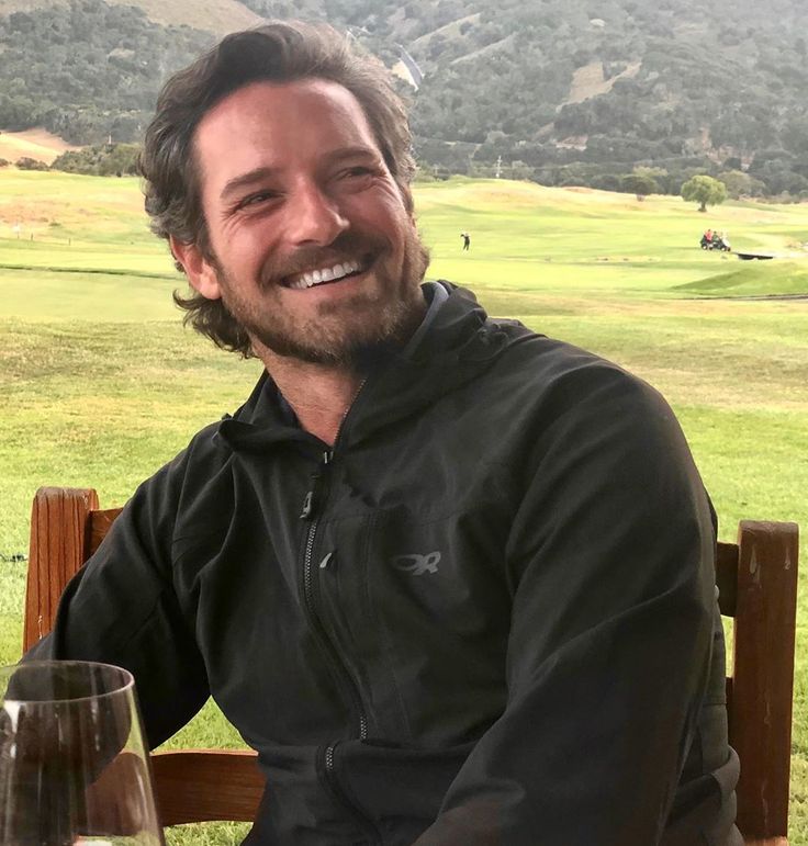 a man sitting at a table with a glass of wine in front of him smiling