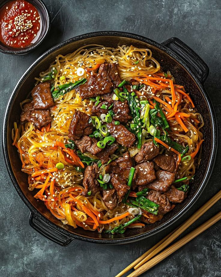 beef and vegetable stir fry in a skillet with chopsticks on the side